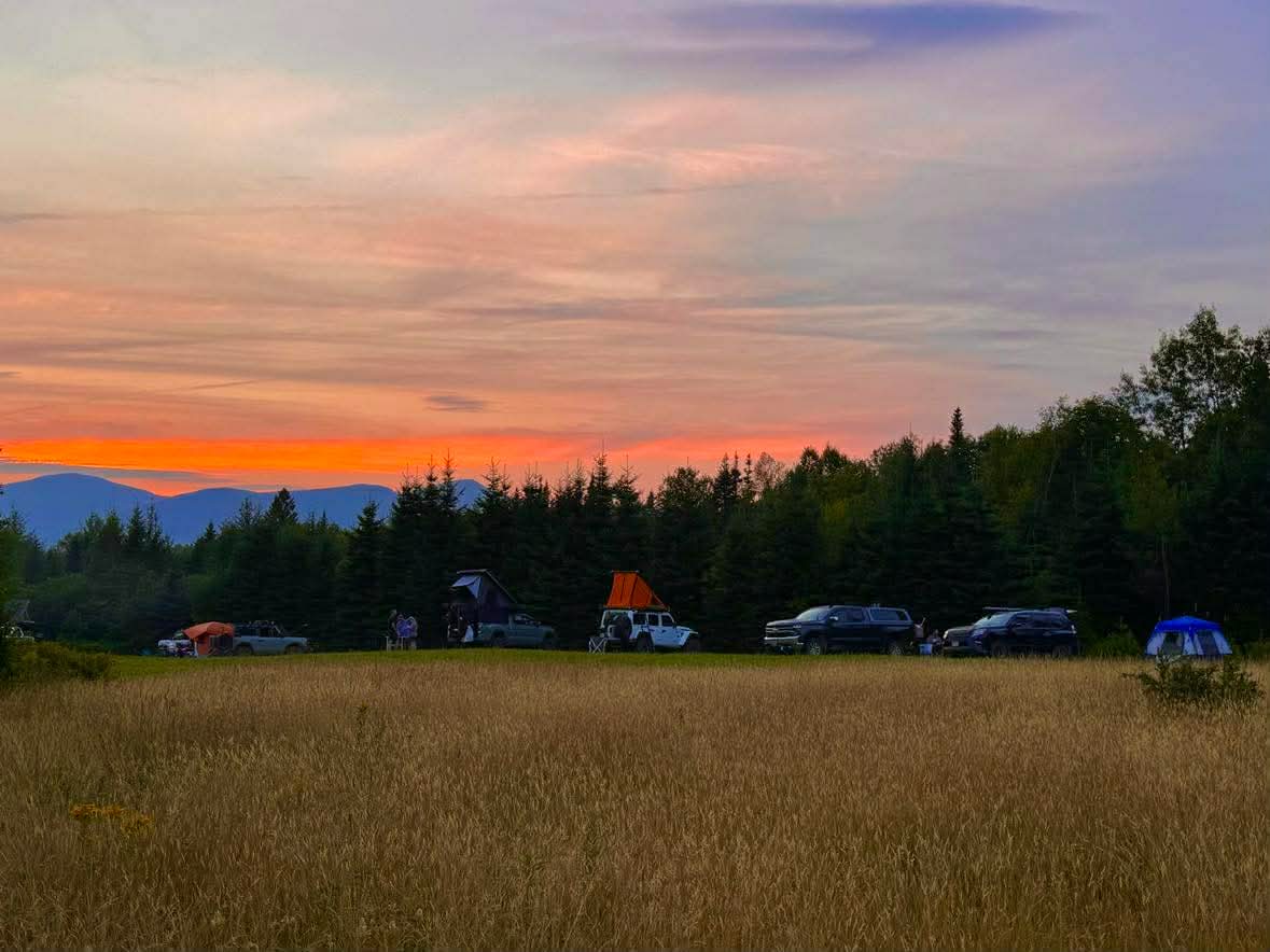 Overland vehicles camped at sunset in a mountain field